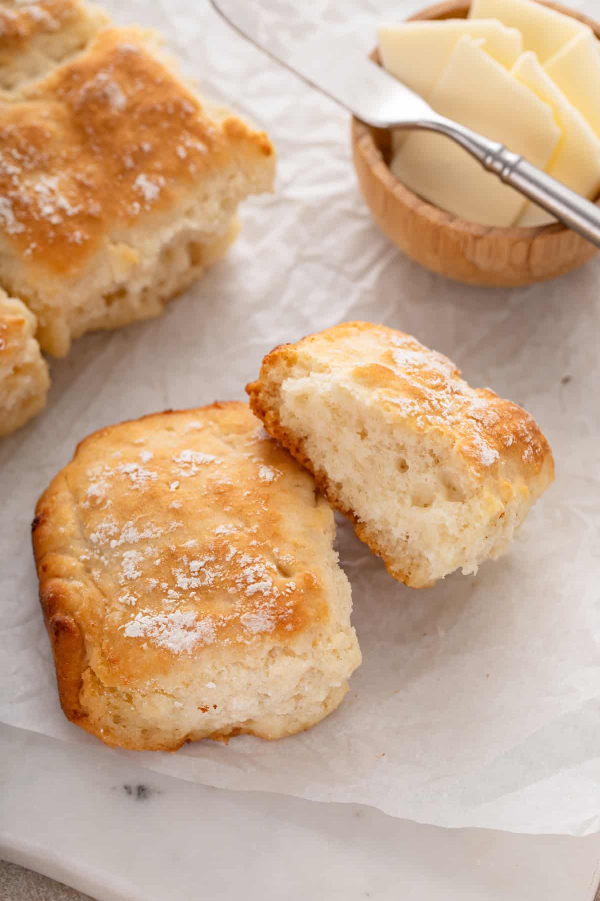 7up biscuits next to a bowl of butter on a piece of parchment paper.