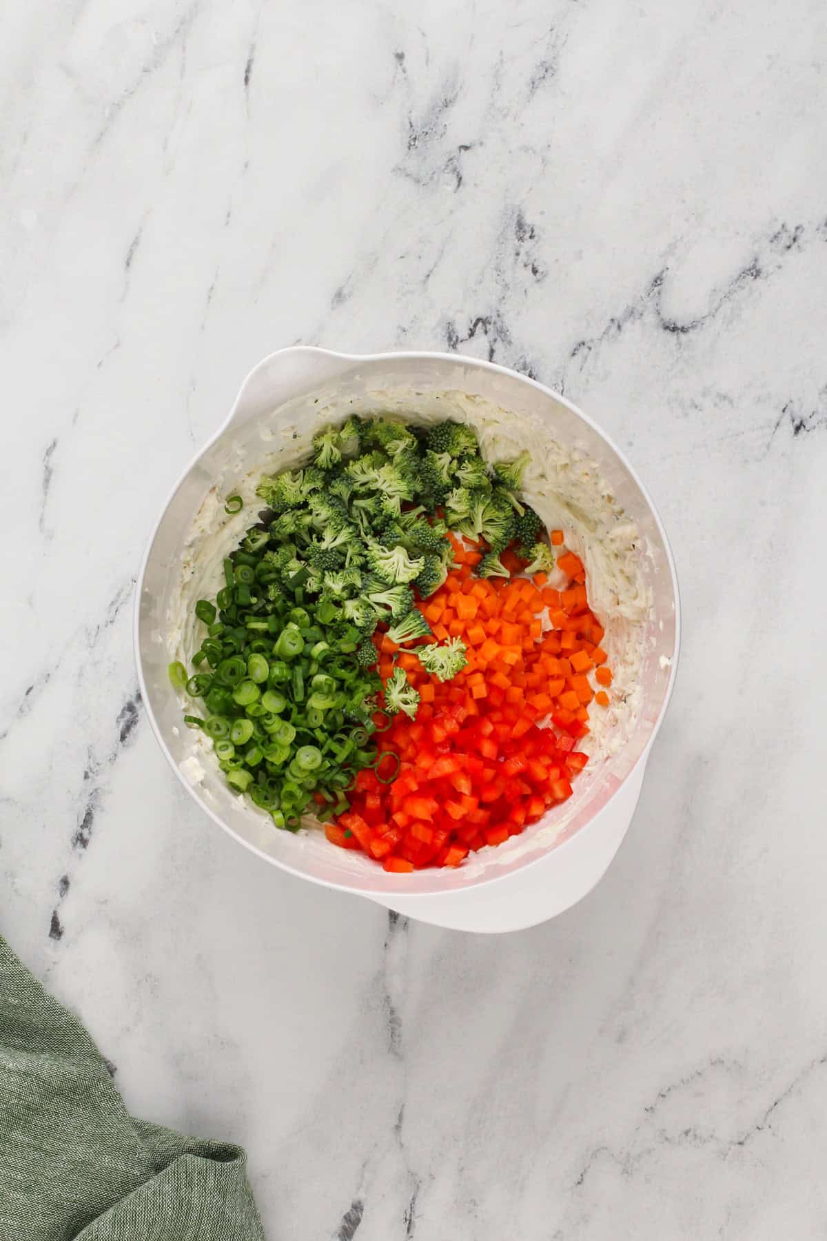 Chopped vegetables added to cream cheese in a white bowl.