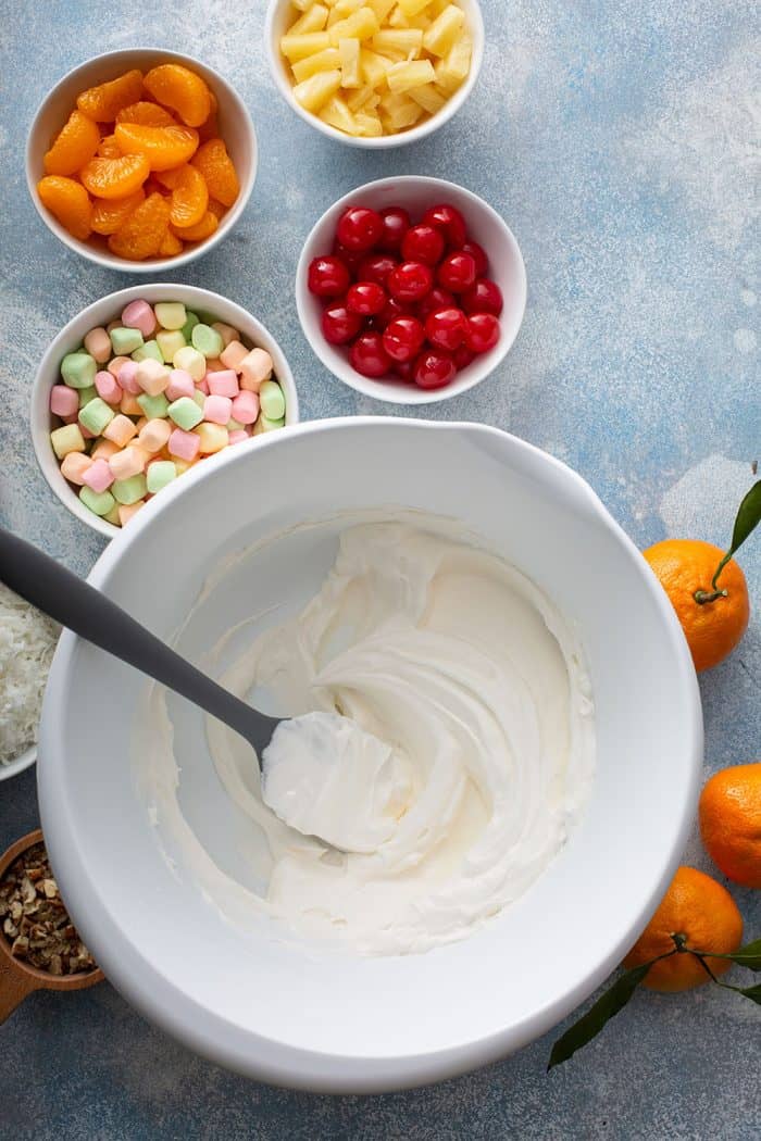 Spatula stirring together the base for ambrosia salad in a white mixing bowl