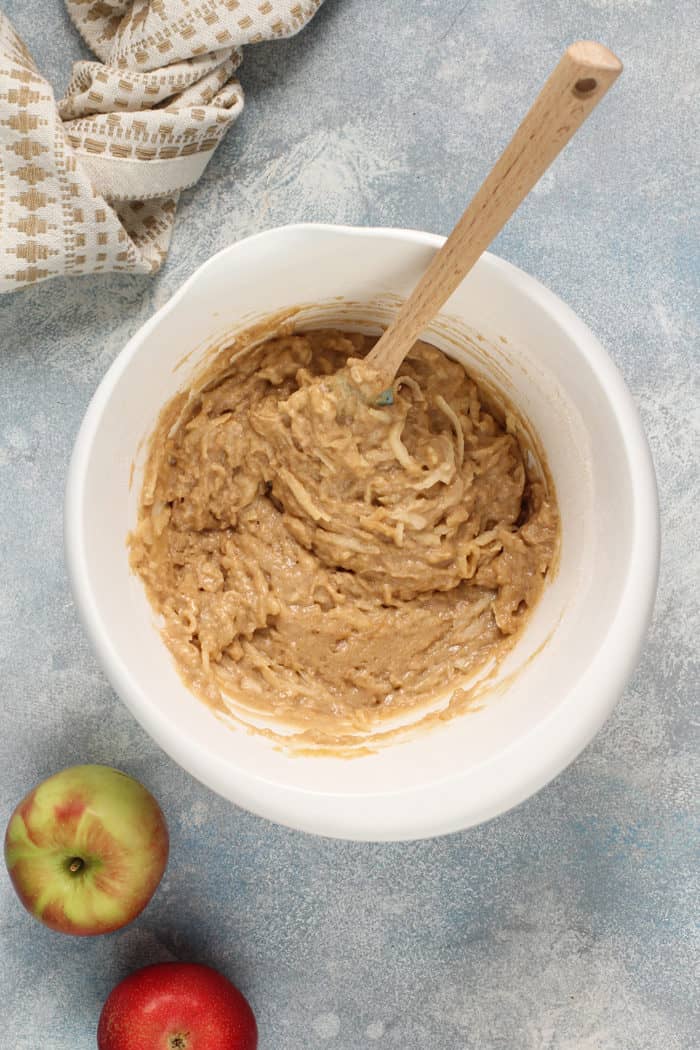 Wooden spoon stirring apple fritter bread batter in a white mixing bowl