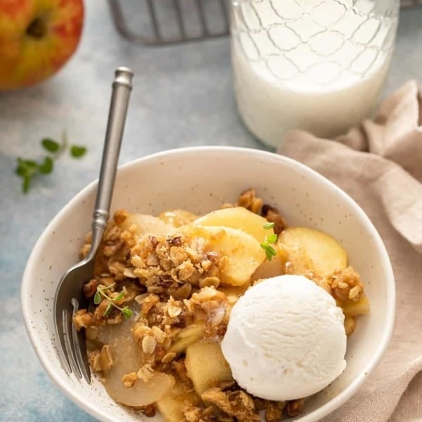 Bowl of apple pear crisp, topped with a scoop of vanilla ice cream, next to a glass of milk