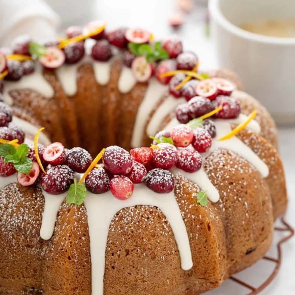 Baked cranberry orange bundt cake topped with glaze, fresh cranberries and orange zest