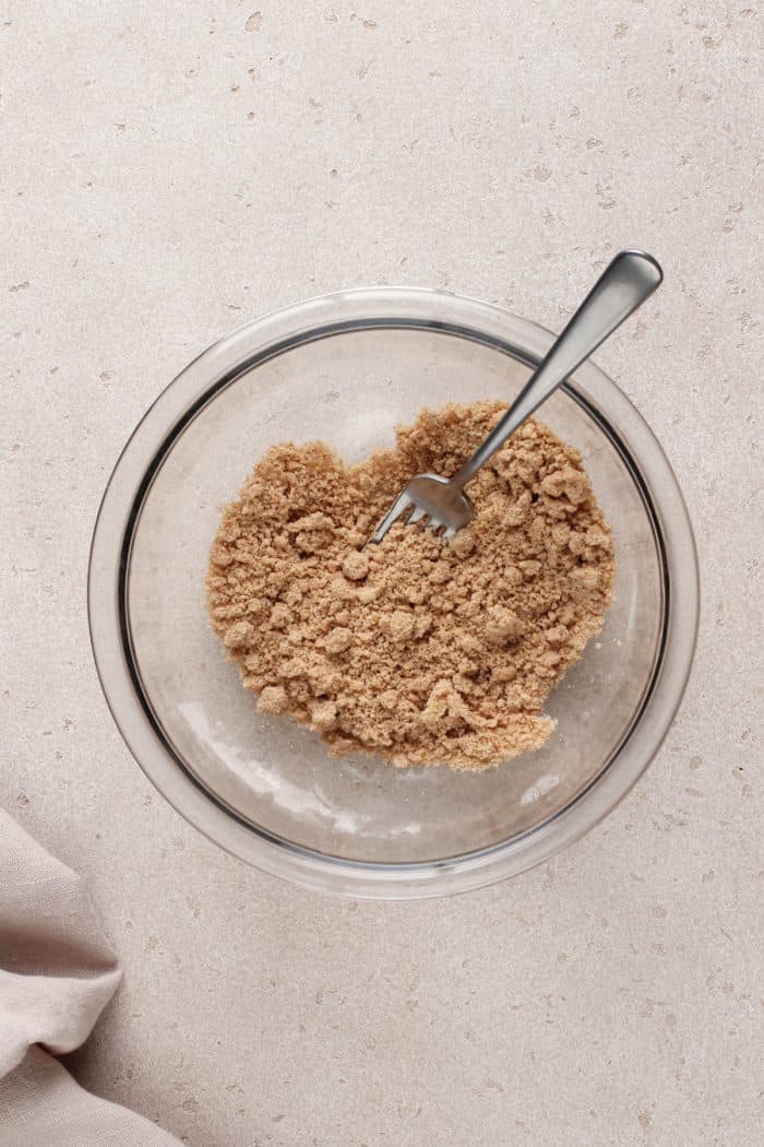 Streusel topping for banana nut bread being stirred together with a fork in a glass bowl.