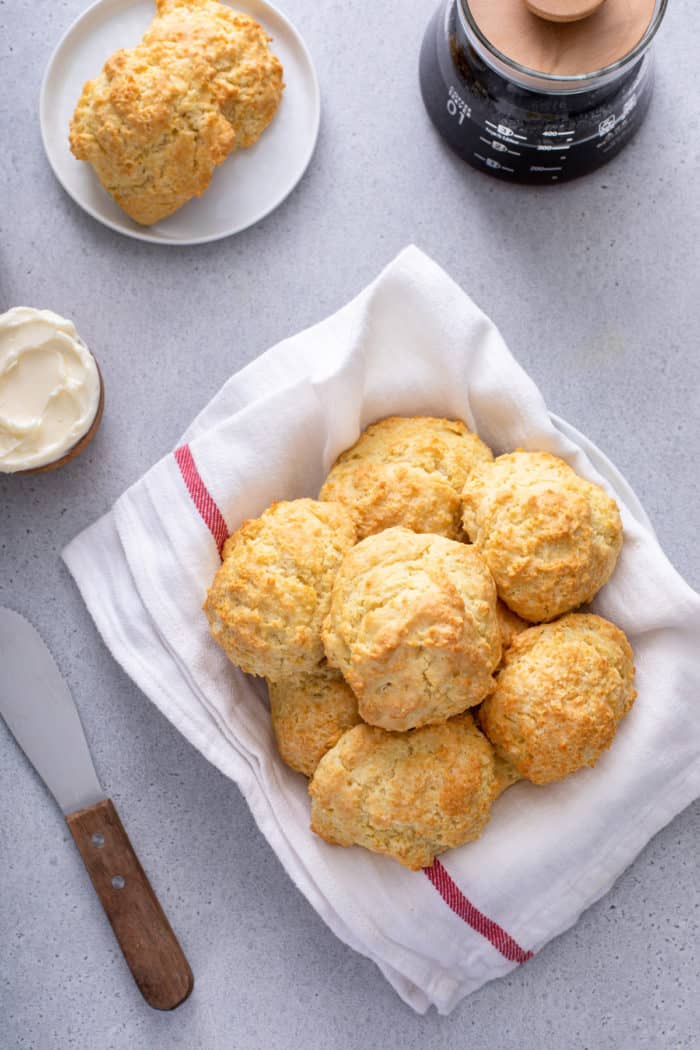 Overhead view of a tea-towel-lined basket filled with buttermilk drop biscuits on a gray countertop.