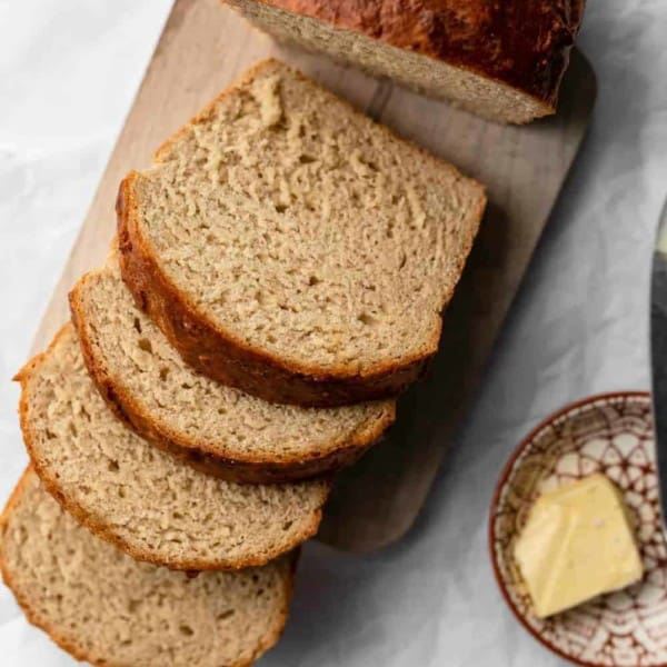 Loaf of beer bread sliced on a wooden cutting board, next to a plate of butter