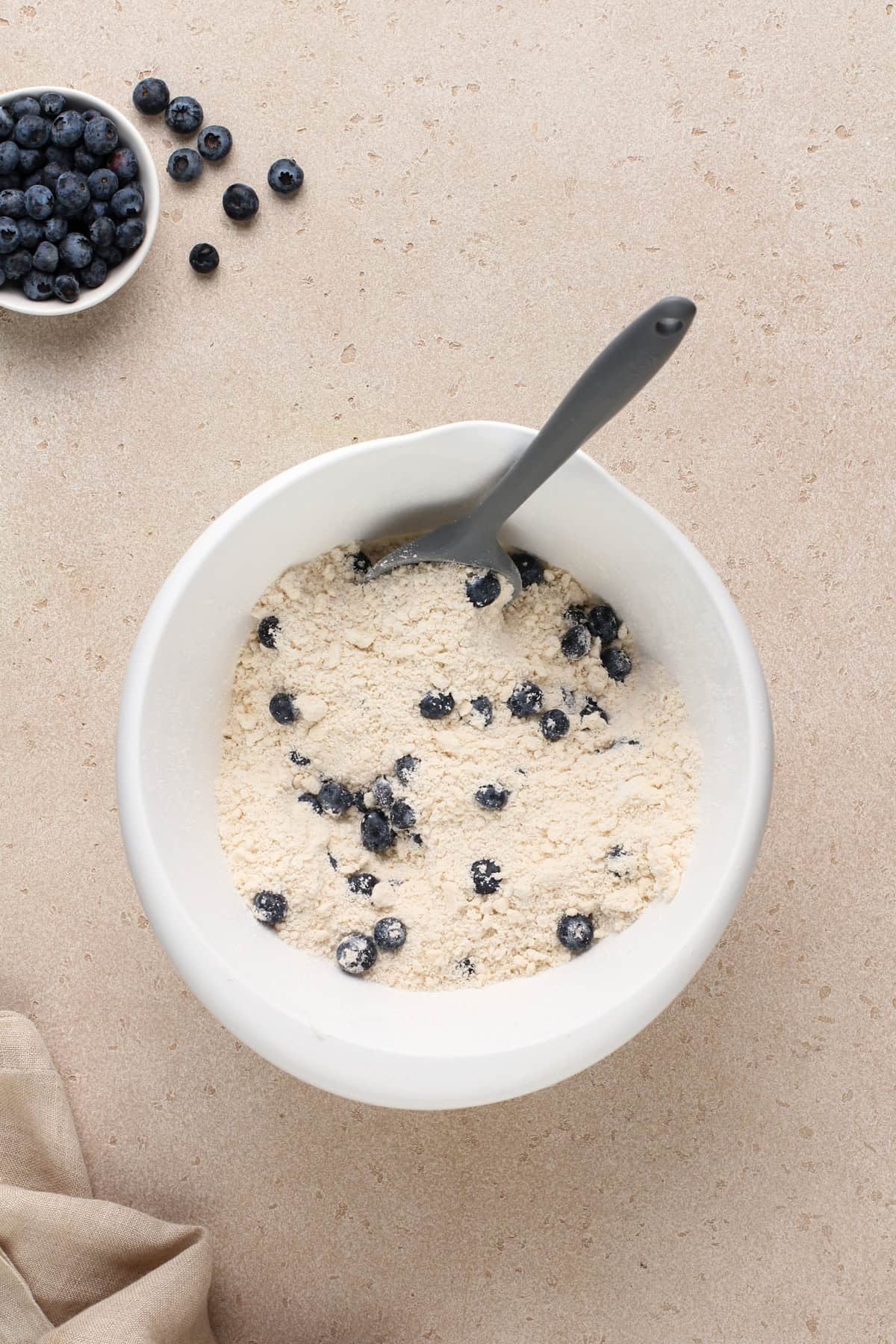 Fresh blueberries tossed with the dry ingredients for blueberry biscuits in a white bowl.