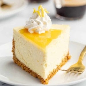 Plated slice of lemon cheesecake next to a fork with espresso in the background