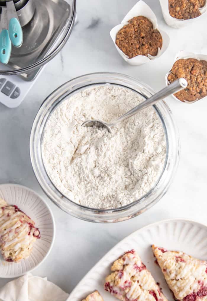 Bowl filled with flour on a marble countertop, surrounded by baked goods.