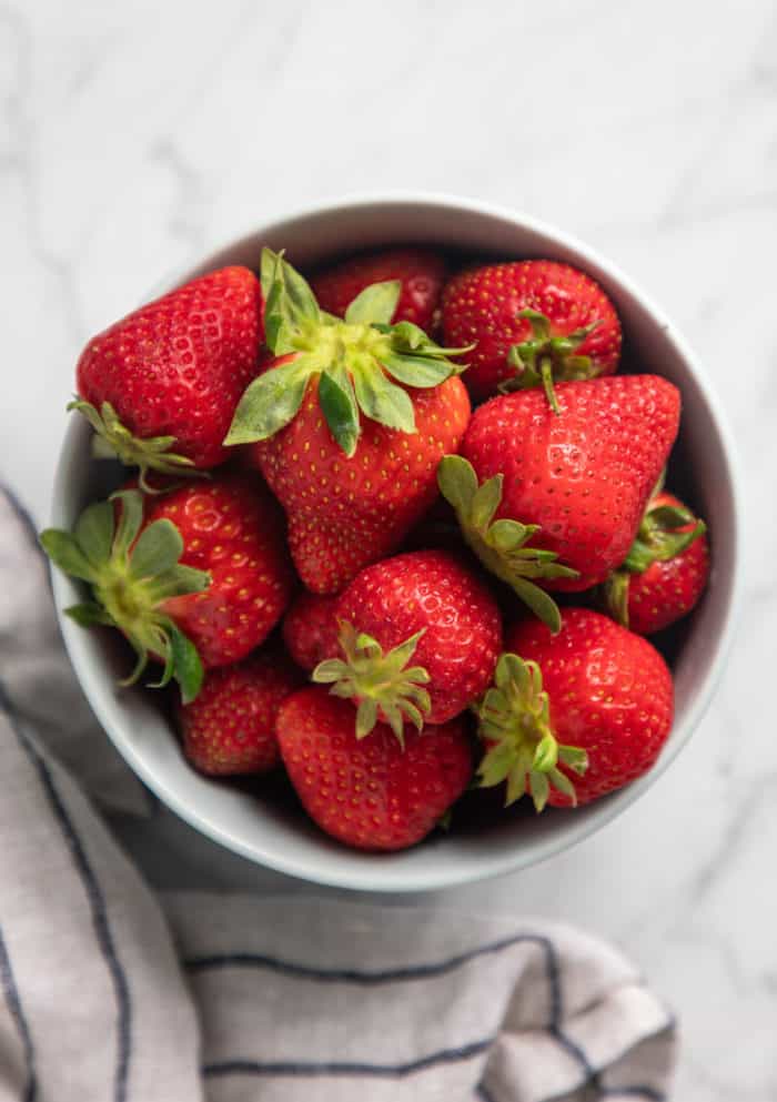 White bowl filled with fresh strawberries set on a marble countertop.