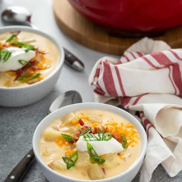 Two bowls of loaded baked potato soup on a counter in front of a dutch oven filled with soup