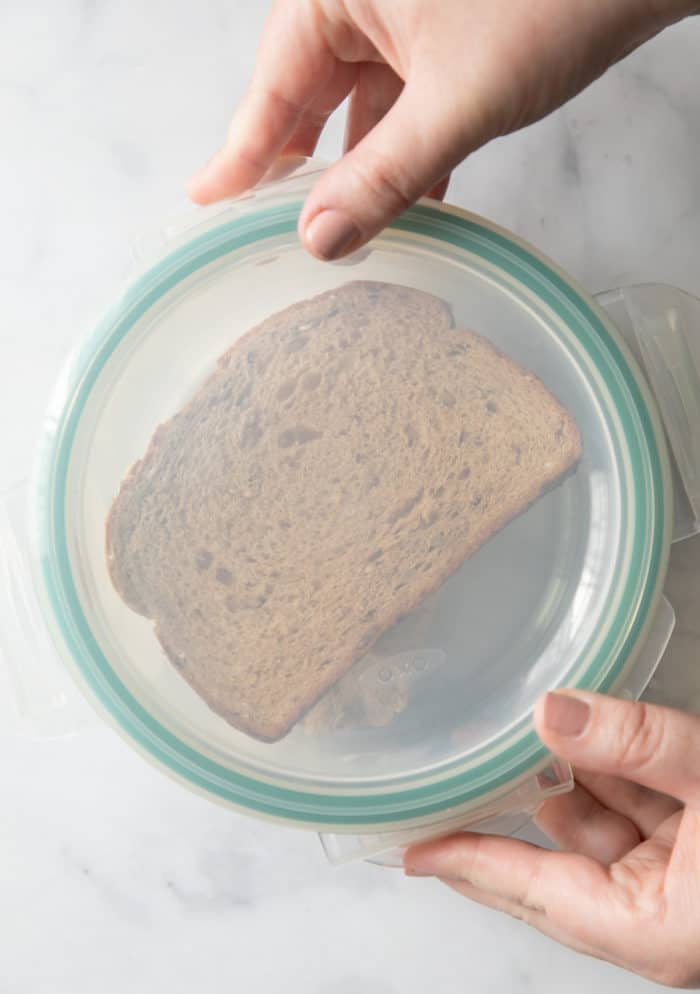 Hand placing a lid on an airtight container. Through the lid you can see a slice of bread inside.