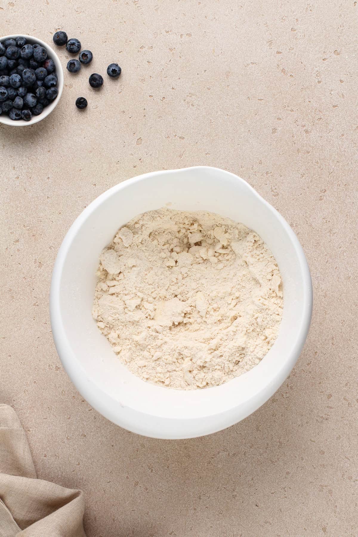 Butter worked into the dry ingredients for blueberry biscuits in a white bowl.