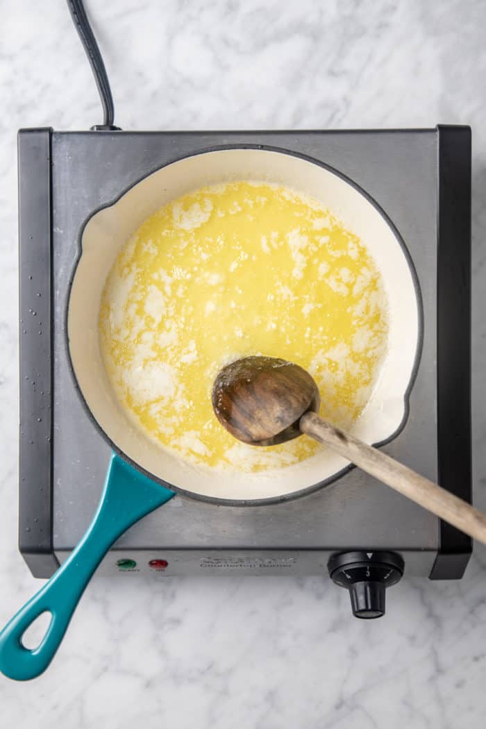 Melted butter that is beginning to foam being stirred with a wooden spoon.