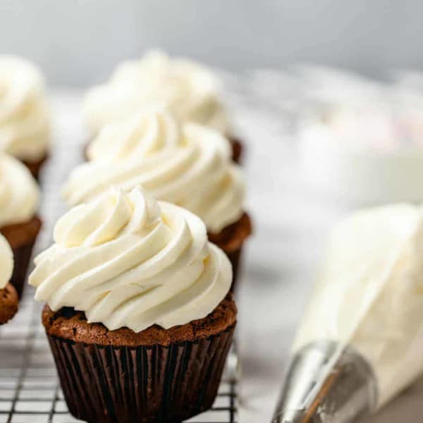 Close up of cupcakes on a cooling rack topped with homemade buttercream frosting