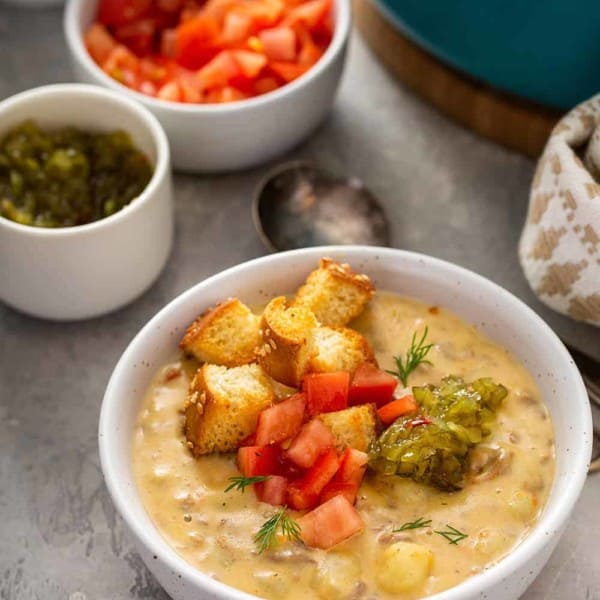 Bowl of cheeseburger soup topped with croutons, diced tomatoes and pickle relish