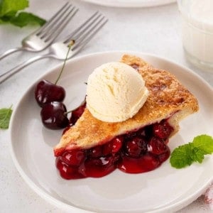 Slice of ice-cream-topped cherry pie on a white plate.