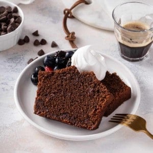 Slice of chocolate bread topped with whipped cream and fresh berries on a white plate.