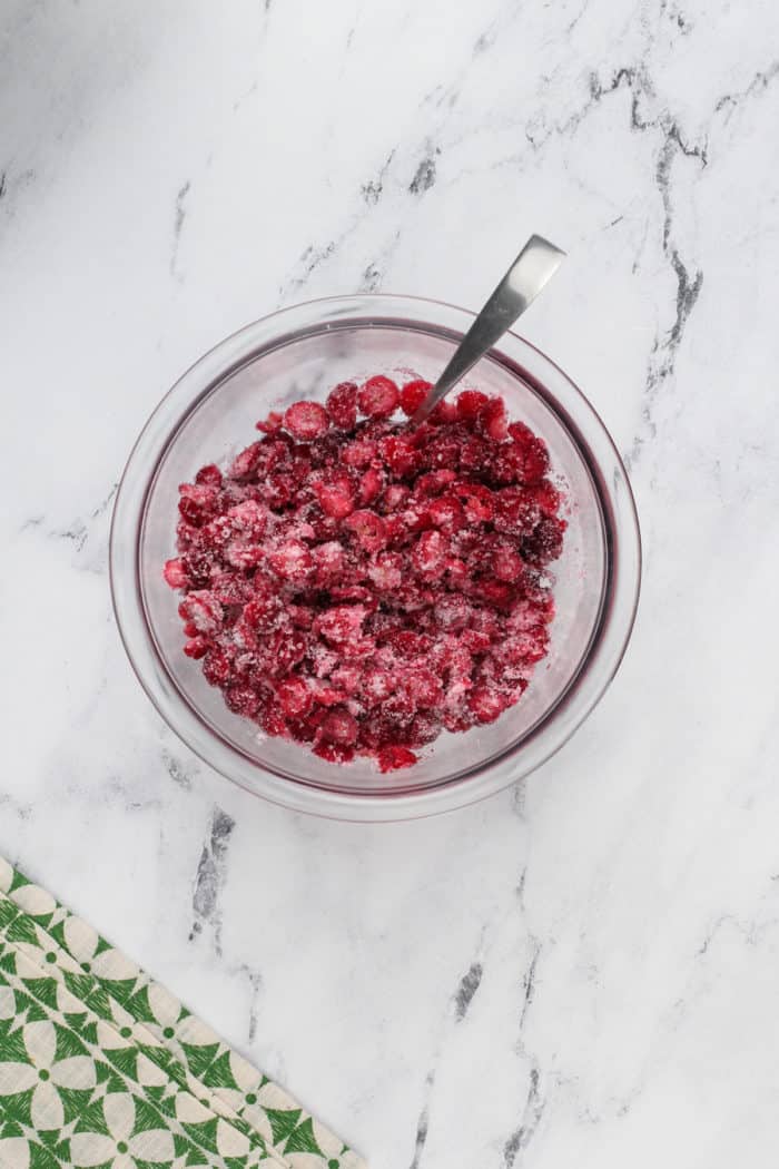 Chopped fresh cranberries tossed with granulated sugar in a glass mixing bowl.