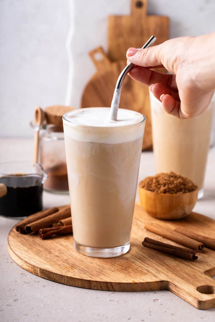 Hand stirring a straw in a glass of iced coffee topped with vanilla sweet cream cold foam.