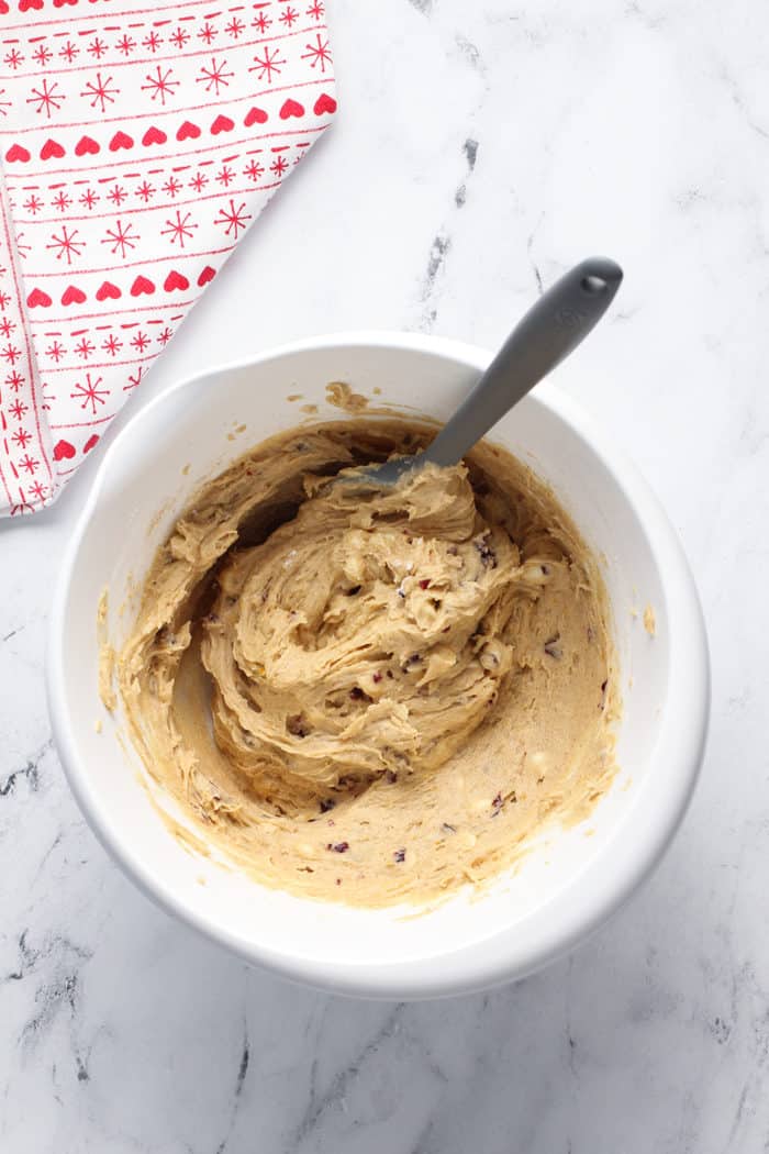 Spatula stirring cranberry bliss bar batter in a white bowl