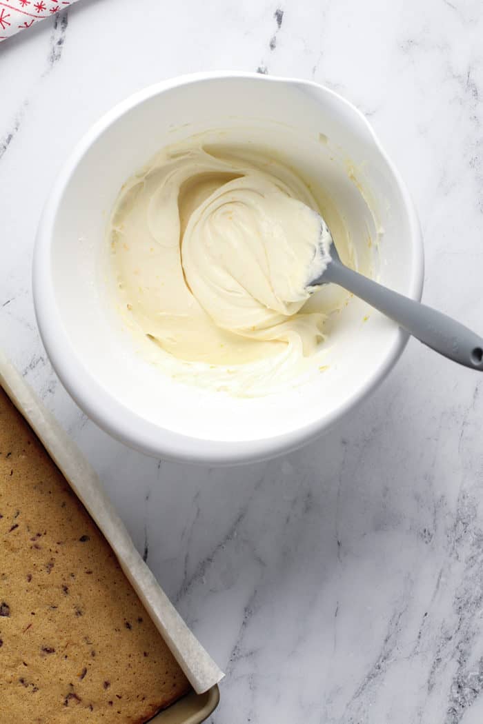 Spatula stirring cream cheese frosting for cranberry bliss bars in a white bowl