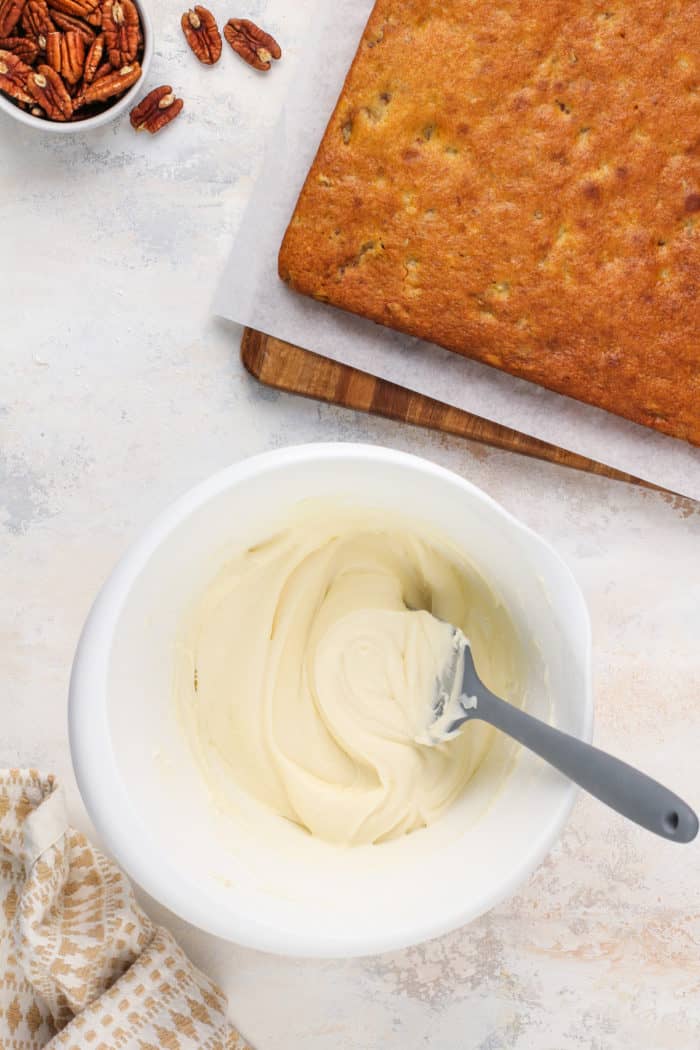 Bowl of cream cheese frosting next to a pan of cooled banana bars.