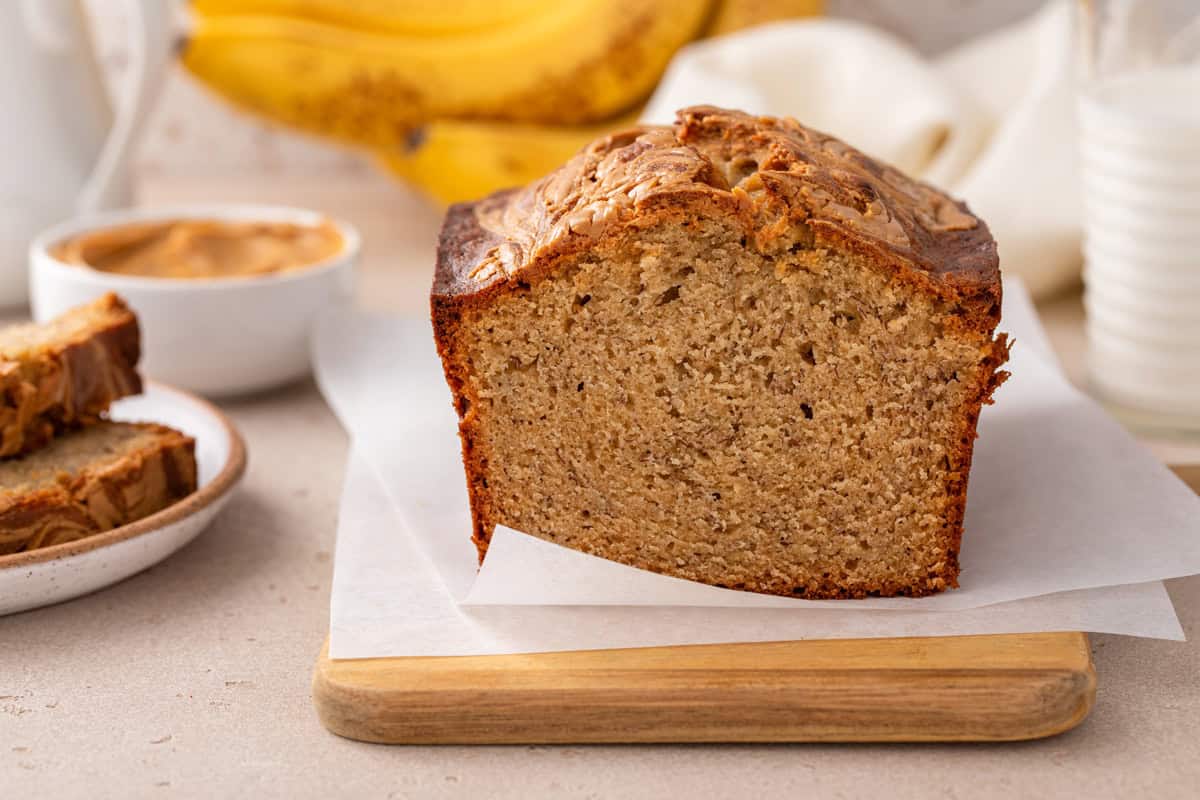 Cut loaf of peanut butter banana bread set on a wooden cutting board to show the cross section.