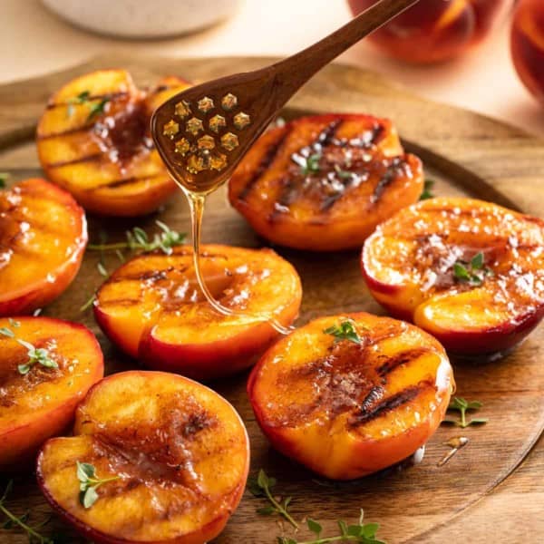 Honey being drizzled over grilled peaches.