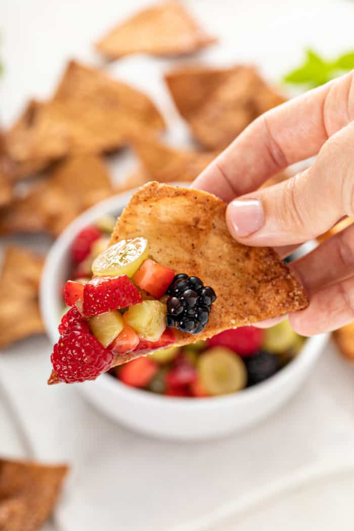 Hand holding up a cinnamon chip with a scoop of fruit salsa on it.