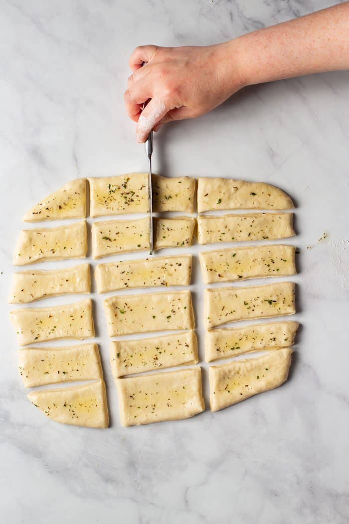 Hand using a paring knife to mark sliced dough for folding into garlic and herb parker house rolls