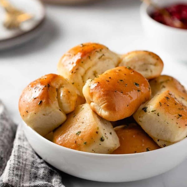 Close up of garlic and herb parker house rolls in a white bowl, set on a marble counter