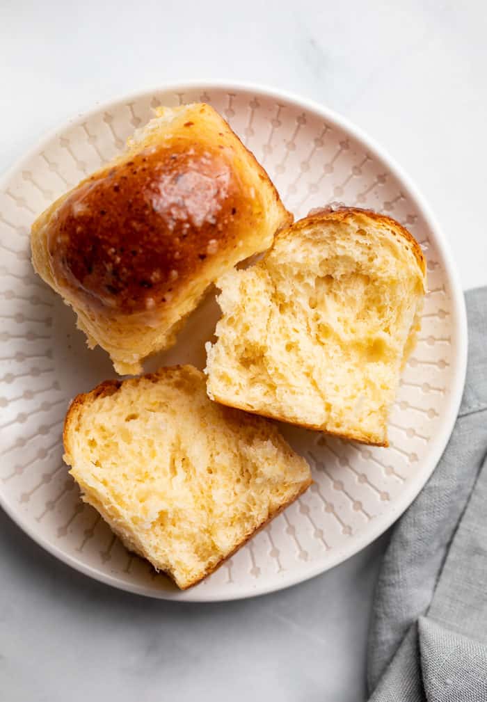 Two cheddar dinner rolls on a white plate. One of them is sliced open to show the fluffy texture inside