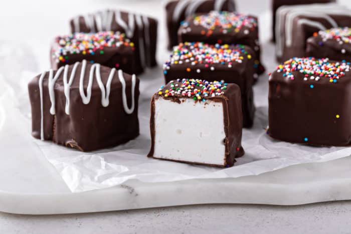 Homemade chococlate-covered marshmallows set on a marble board. One of the marshmallows has been cut in half.