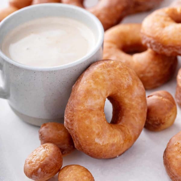 Homemade doughnut resting against the side of a cup of coffee.