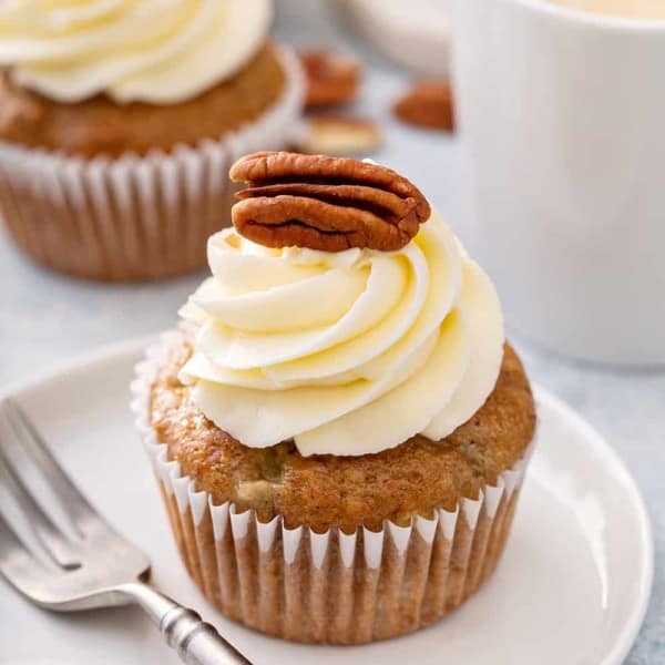 Frosted hummingbird cupcake next to a fork on a white plate