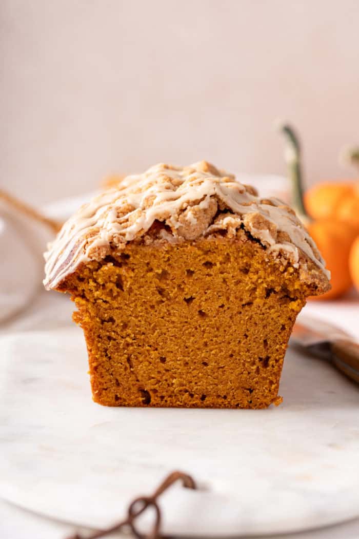 Side view of the cut edge of a loaf of streusel-topped pumpkin bread with maple glaze.