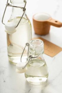 A large and small bottle of simple syrup with a measuring cup of sugar in the background