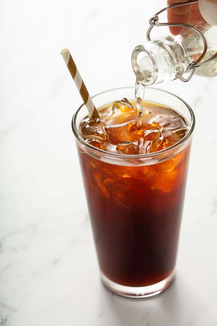 Simple syrup being poured from a small bottle into a glass of iced coffee