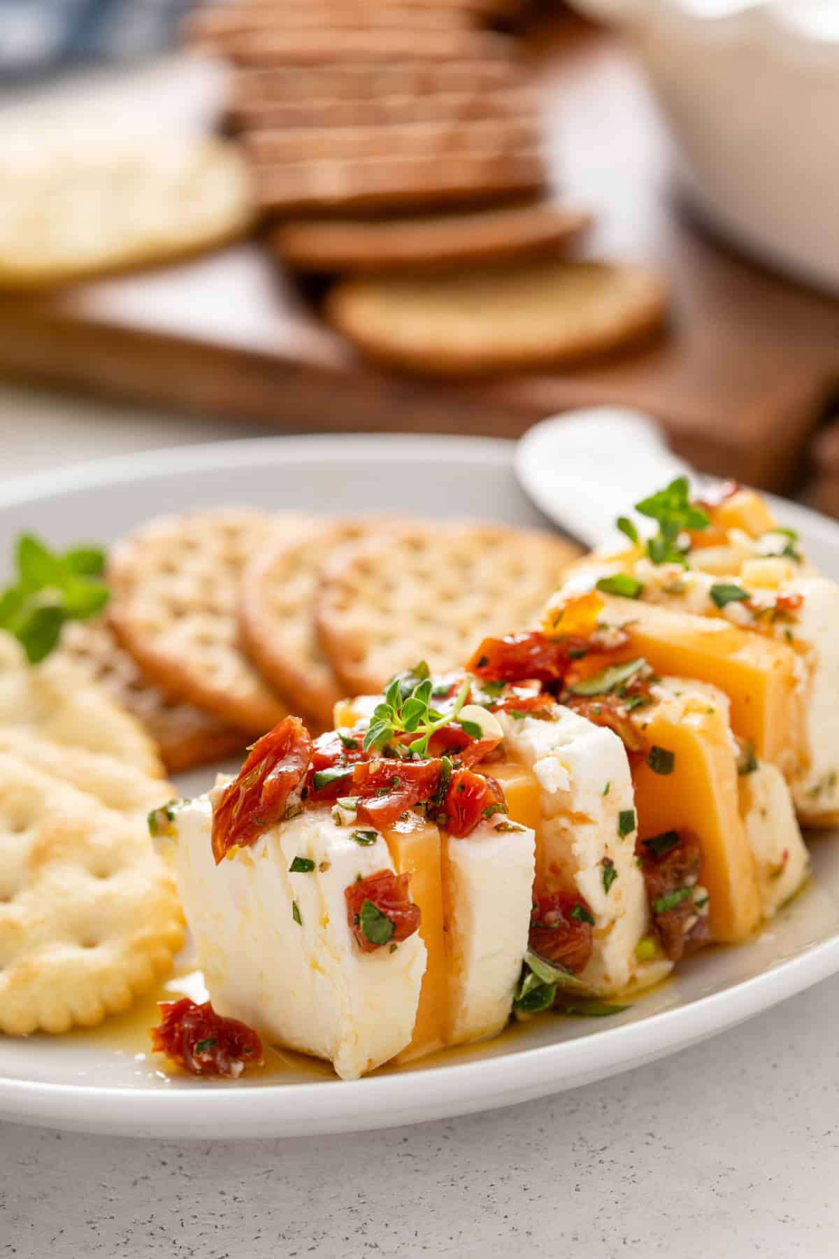 Close up of marinated cheese next to crackers on a white plate.