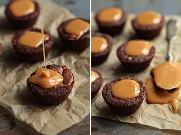 Milky Way brownie bites getting caramel drizzled on top next to a spoon on parchment paper