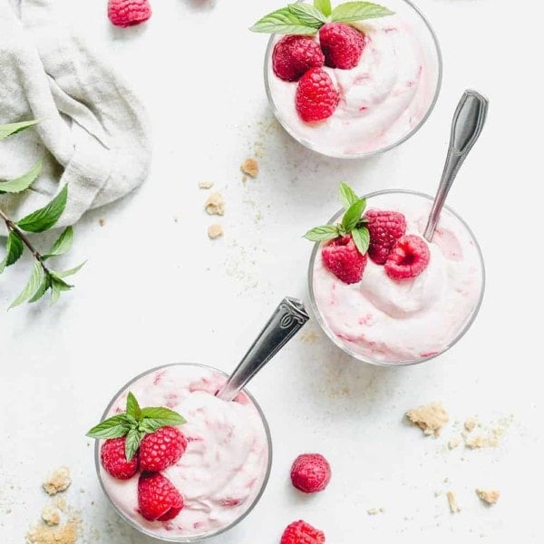 Overhead view of three bowls of no-bake raspberry lemon cheesecakes garnished with fresh raspberries and mint on a marble countertop