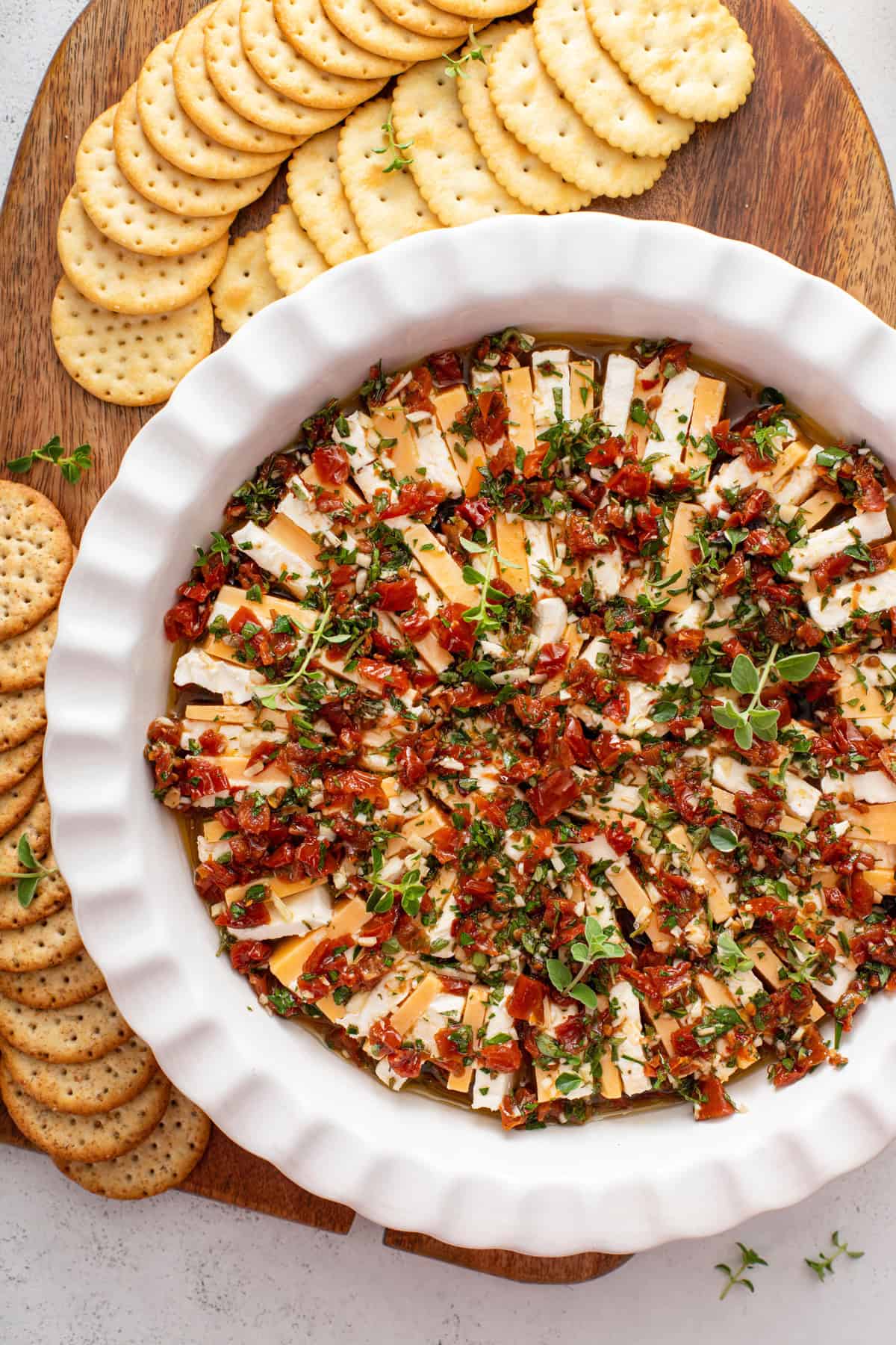 Overhead view of marinated cheese in a white serving dish on a platter surrounded by crackers.