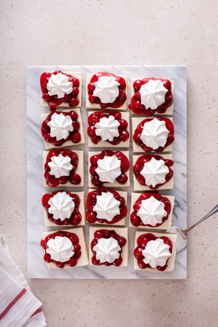 Overhead view of sliced nana's easy cheesecake on a marble board. The slices are topped with cherry pie filling and whipped topping.