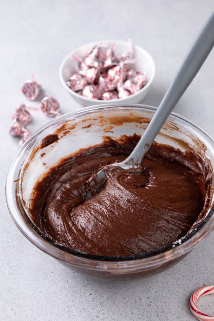 Peppermint brownie batter being stirred with a spatula in a glass mixing bowl.