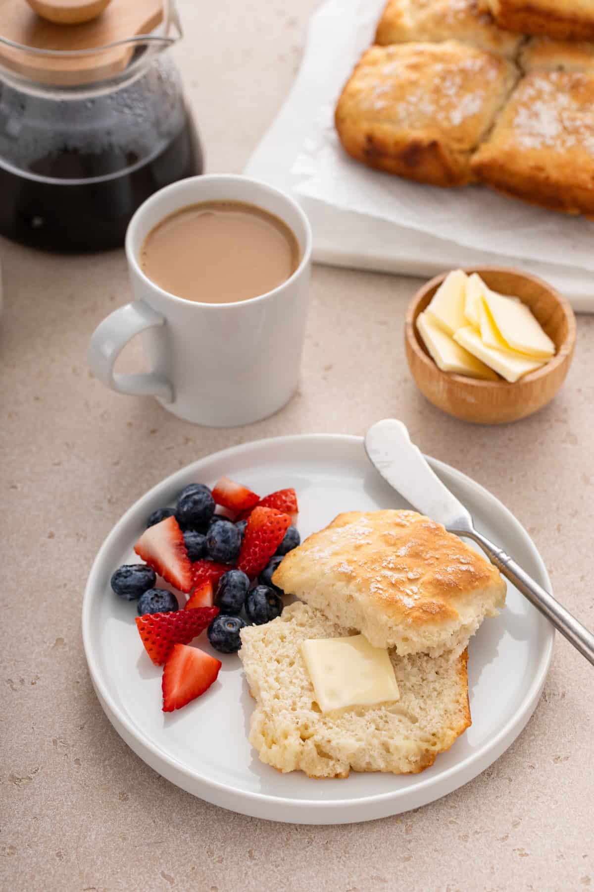 Buttered 7up biscuit next to fresh berries on a white plate.