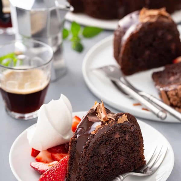 Plates of easy chocolate bundt cake next to a cake plate and cups of espresso