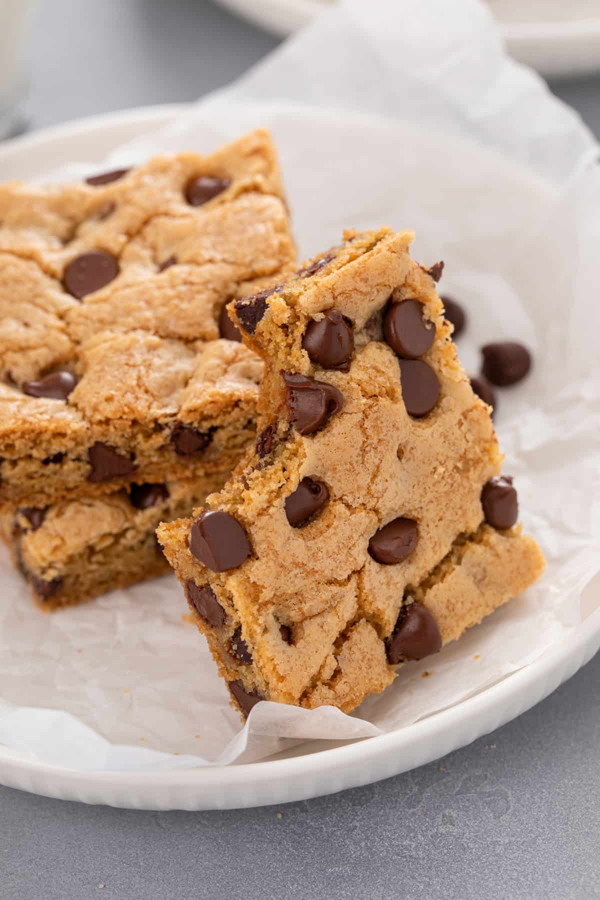 Chocolate chip cookie bar with a bite taken from it leaning against a stack of cookie bars on a white plate.