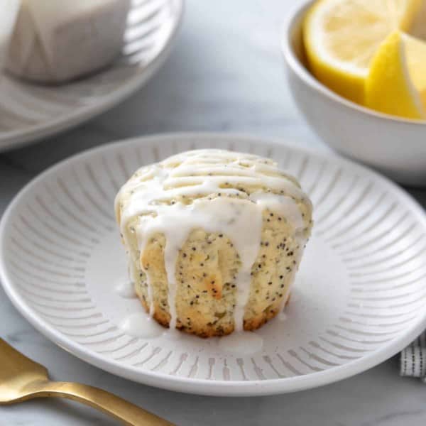 Glazed lemon poppy seed muffin set on a white plate.