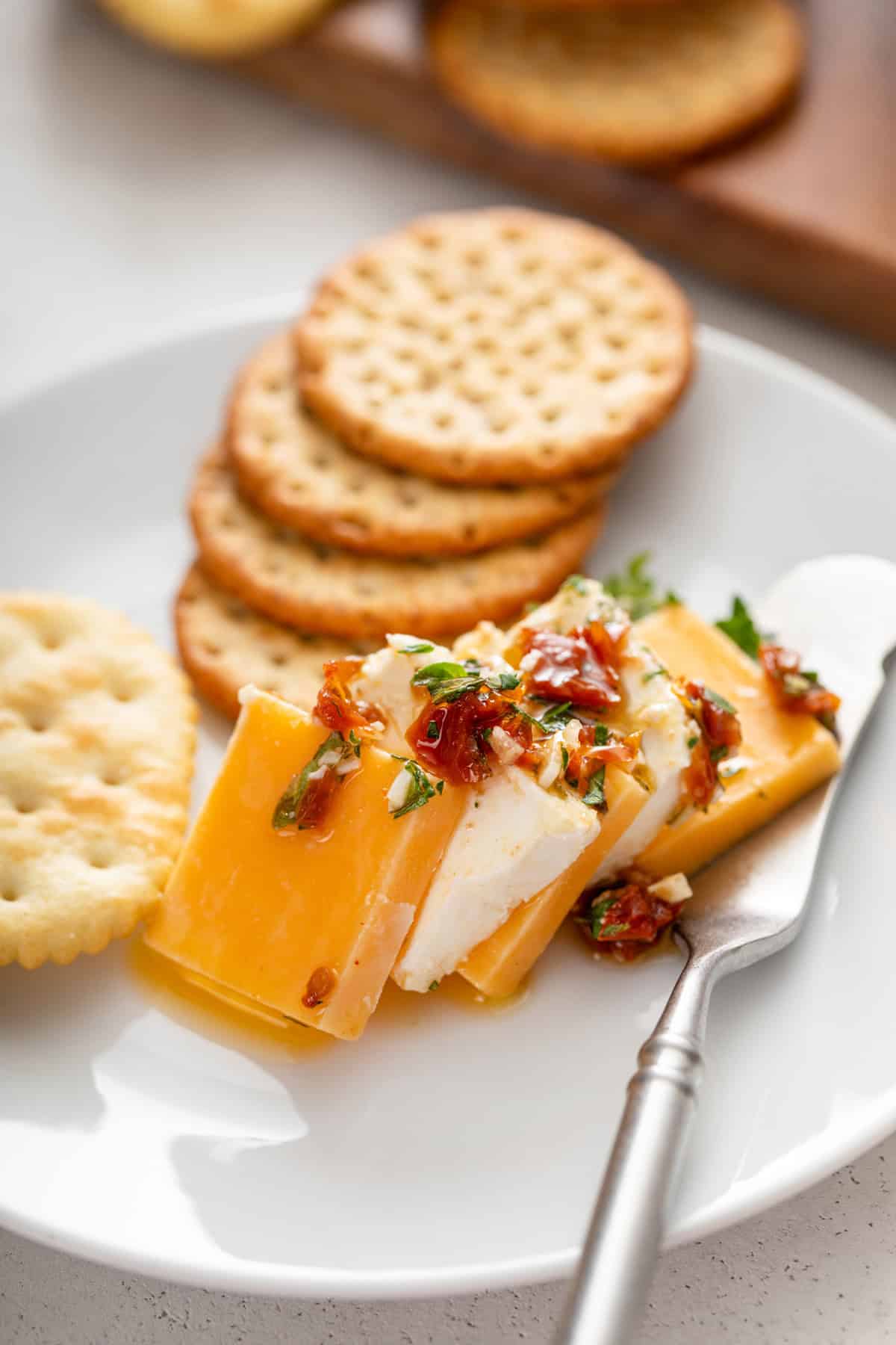 Several pieces of marinated cheese next to crackers on a white plate.