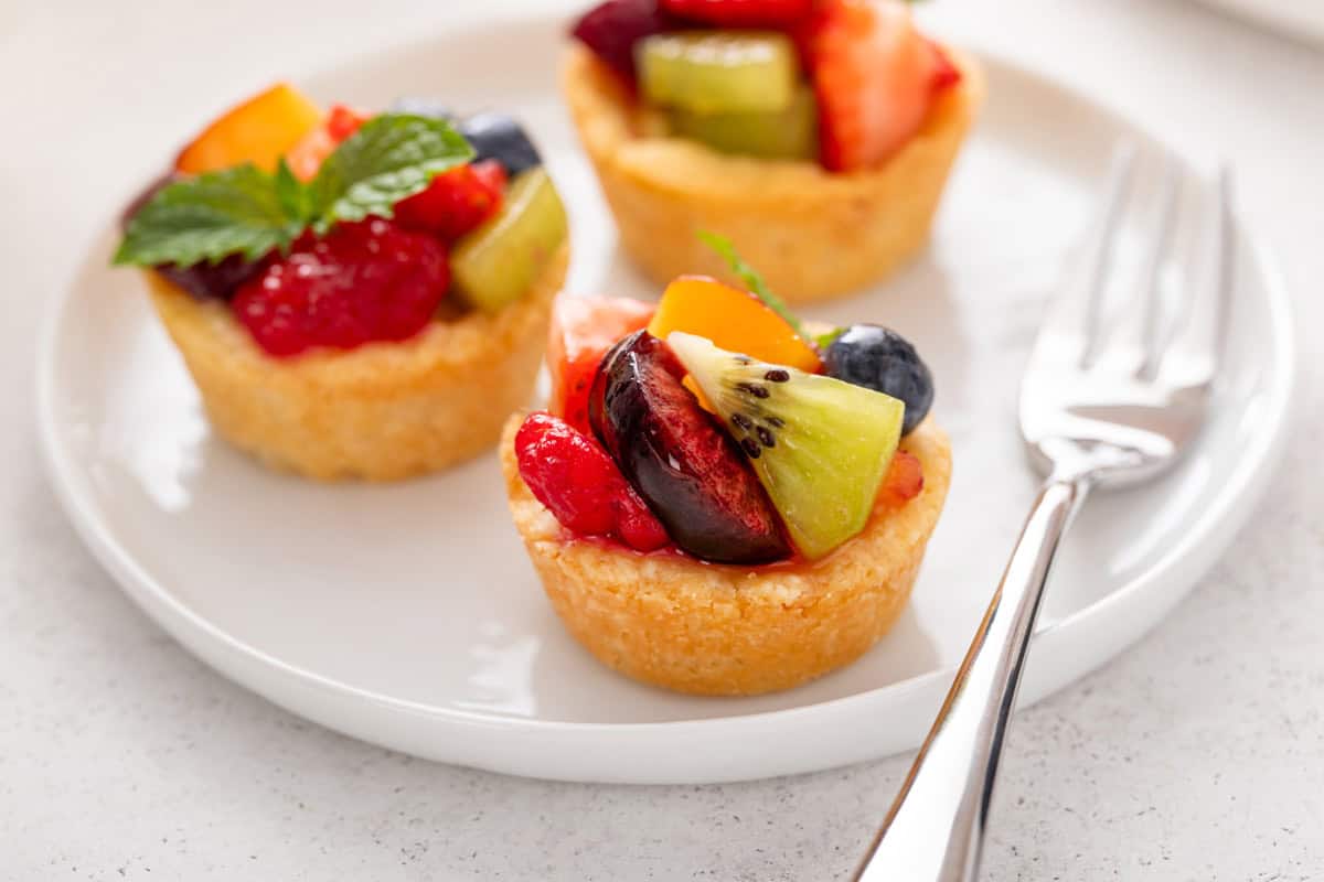 Three mini fruit tarts arranged on a white plate.